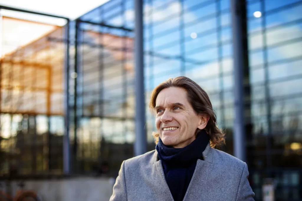 Mertzi katsoo hymyillen ylöspäin. Hänellä on takki ja kaulaliina, taustalla näkyy lasinen rakennus. Kuvan ottanut Susanna Kekkonen.